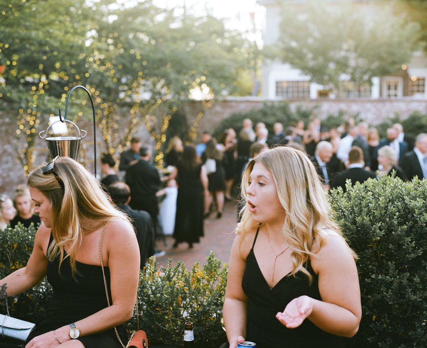 Guests enjoying an elegant outdoor party with black attire and garden greenery.
