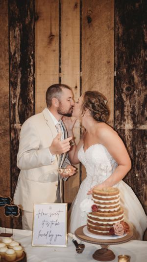 Newlyweds sharing cake cutting moment at rustic wedding with wooden wall backdrop.
