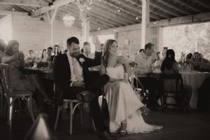Wedding guests dancing and celebrating at a rustic indoor reception venue with string lights overhead.
