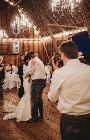 Couples dancing in a rustic barn venue with elegant chandeliers hanging from wooden beams.