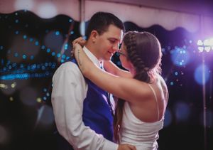 A tender slow dance moment at a wedding reception with blue lighting.