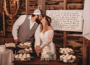 A couple sharing a sweet moment at their rustic wedding dessert table with handwritten signage.