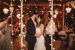 Wedding reception in rustic barn venue with hanging string lights creating warm ambiance.