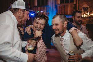 Groomsmen laughing and celebrating at wedding reception with drinks.