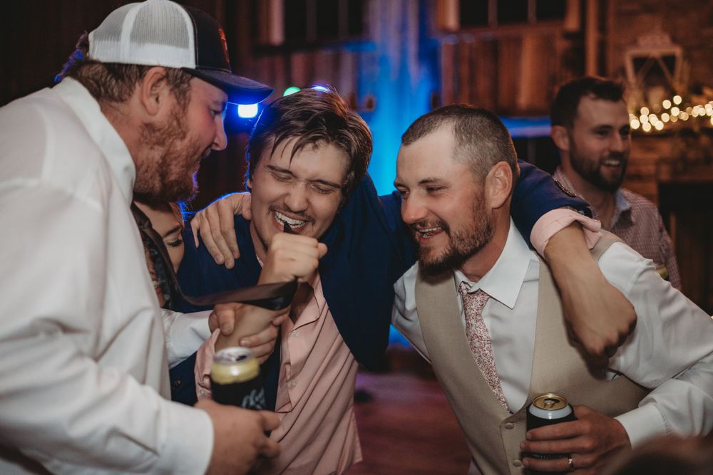 Groomsmen laughing and celebrating at wedding reception with drinks.
