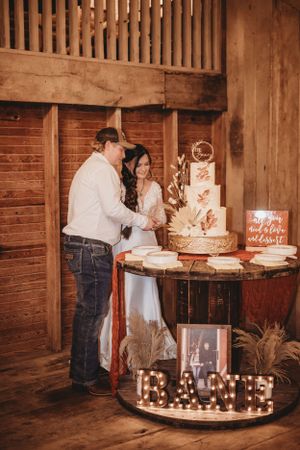 Wedding cake cutting ceremony in a rustic barn setting with wooden walls and warm lighting.