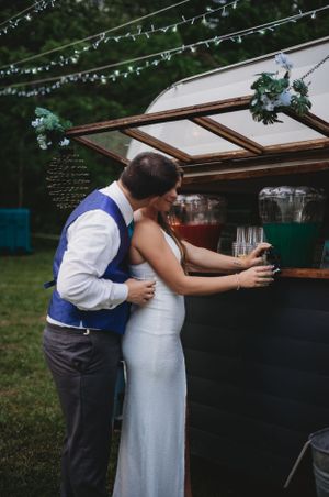 A couple sharing an intimate moment at an outdoor wedding bar under string lights.