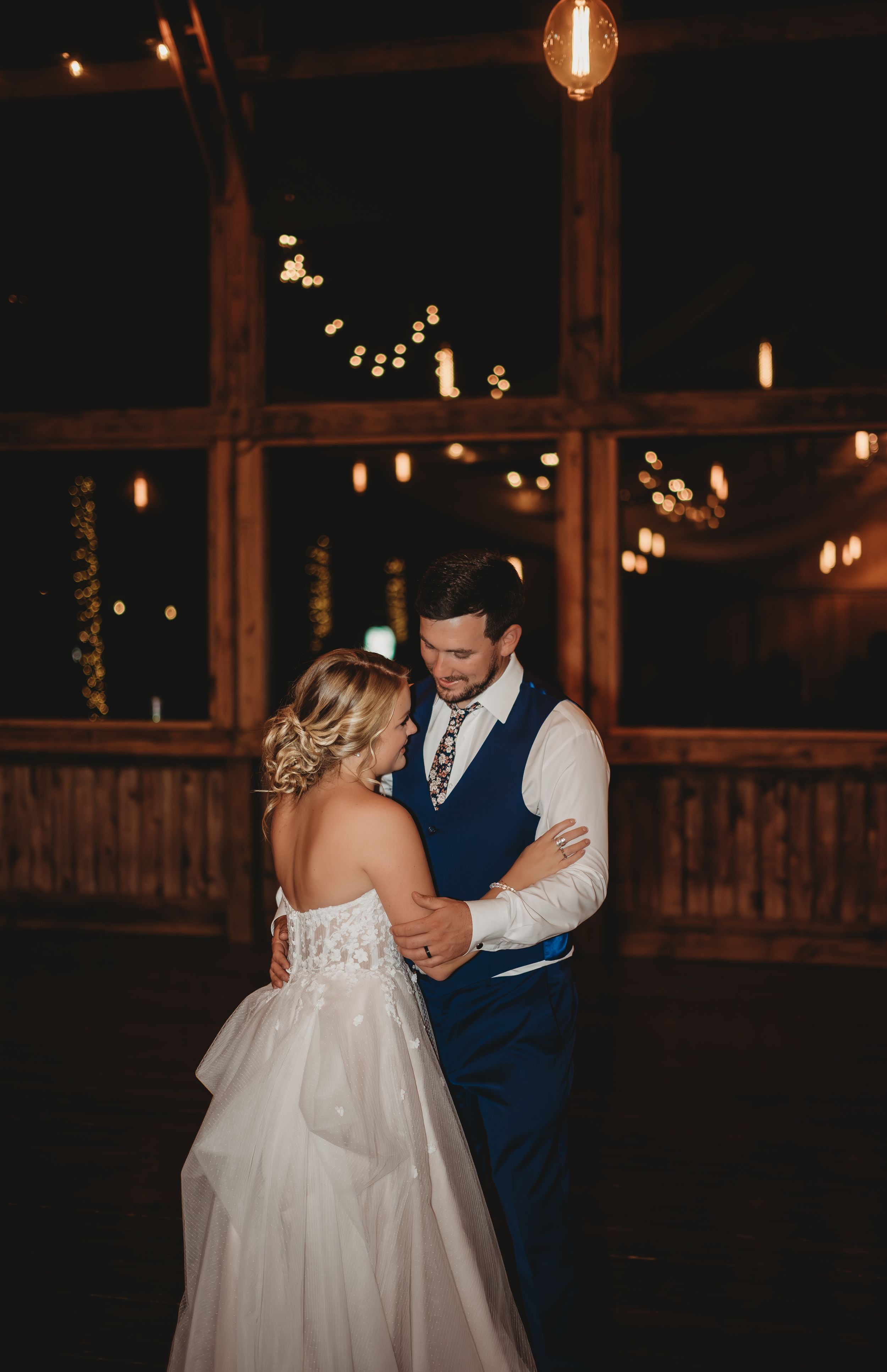A romantic first dance at a rustic wedding venue illuminated by string lights.