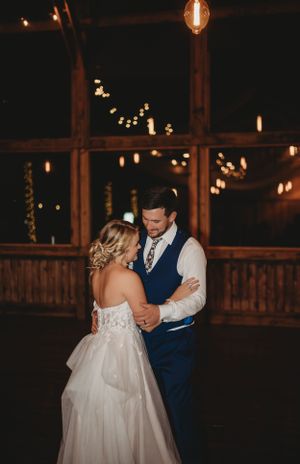 A romantic first dance at a rustic wedding venue illuminated by string lights.
