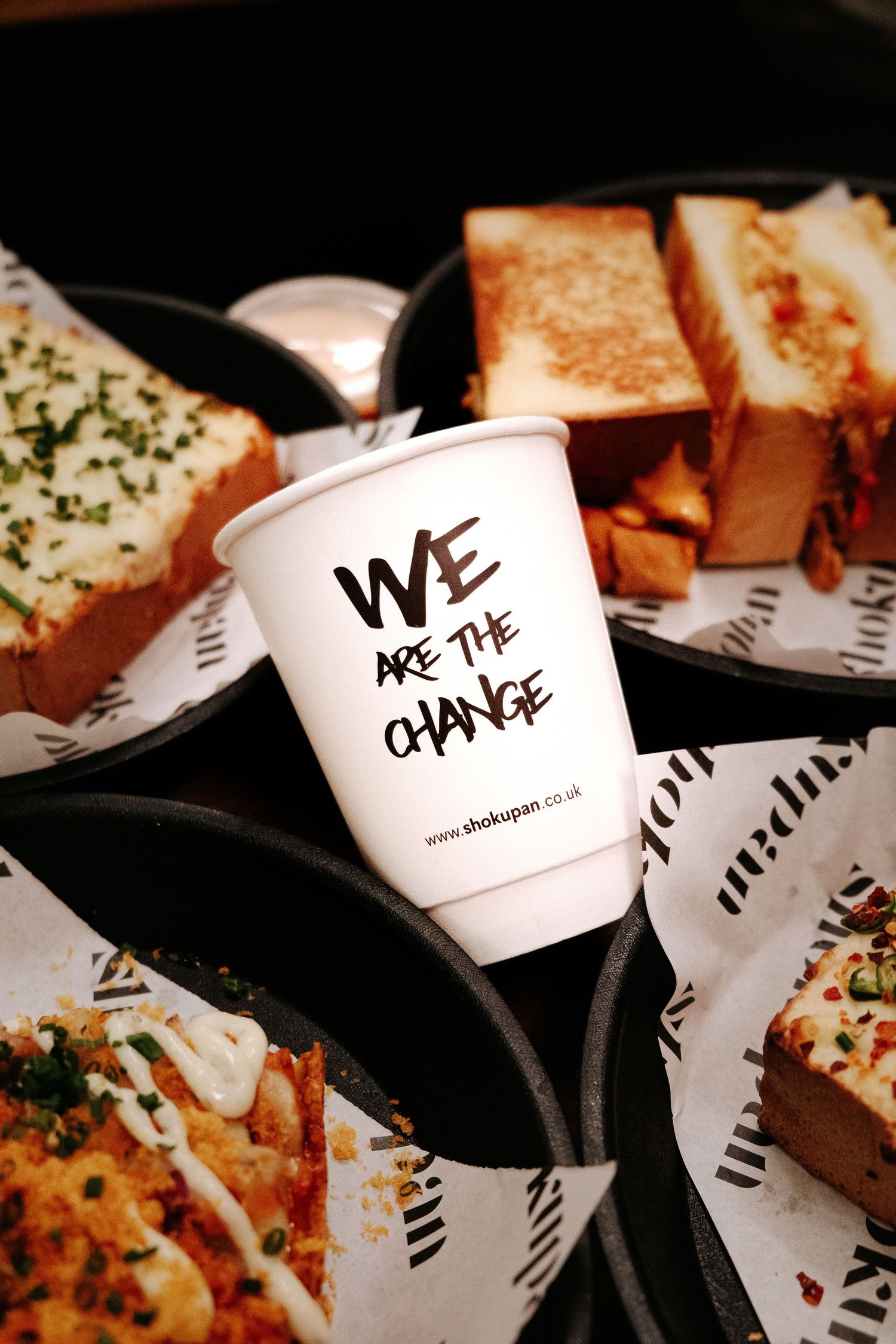 Shokupan cup, with we are the change written on it, placed amongst numerous Japanese sandos sandwiches.