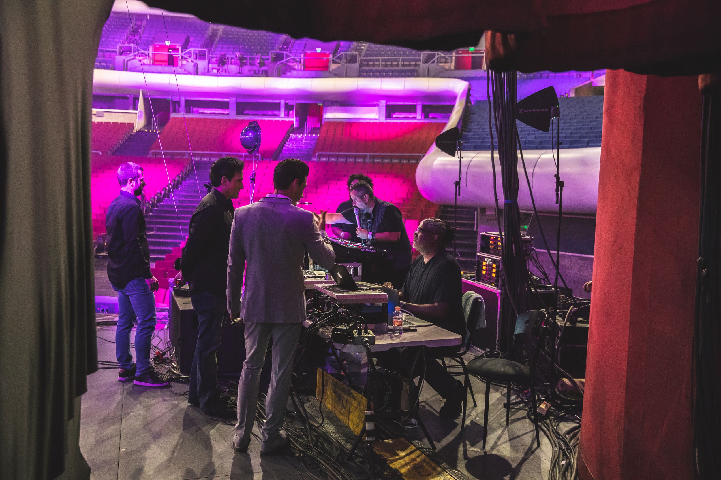 Backstage area lit with purple and red ambient lighting showing technical equipment and crew.