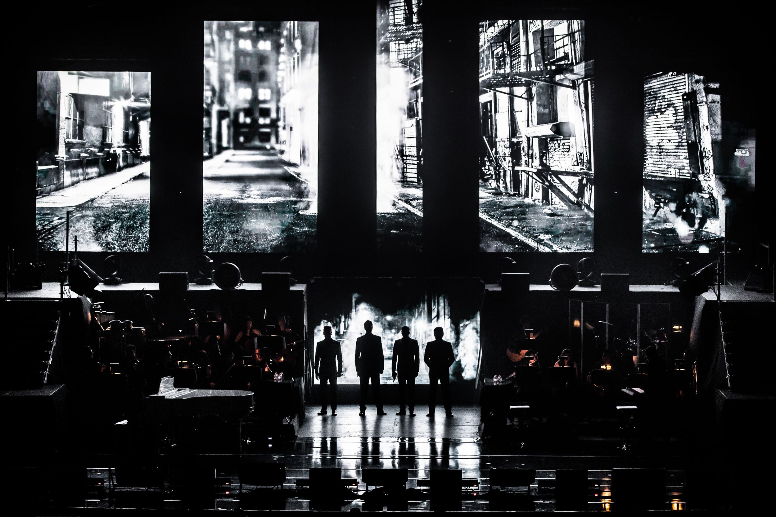 Silhouetted figures perform on stage with dramatic black and white lighting effects.