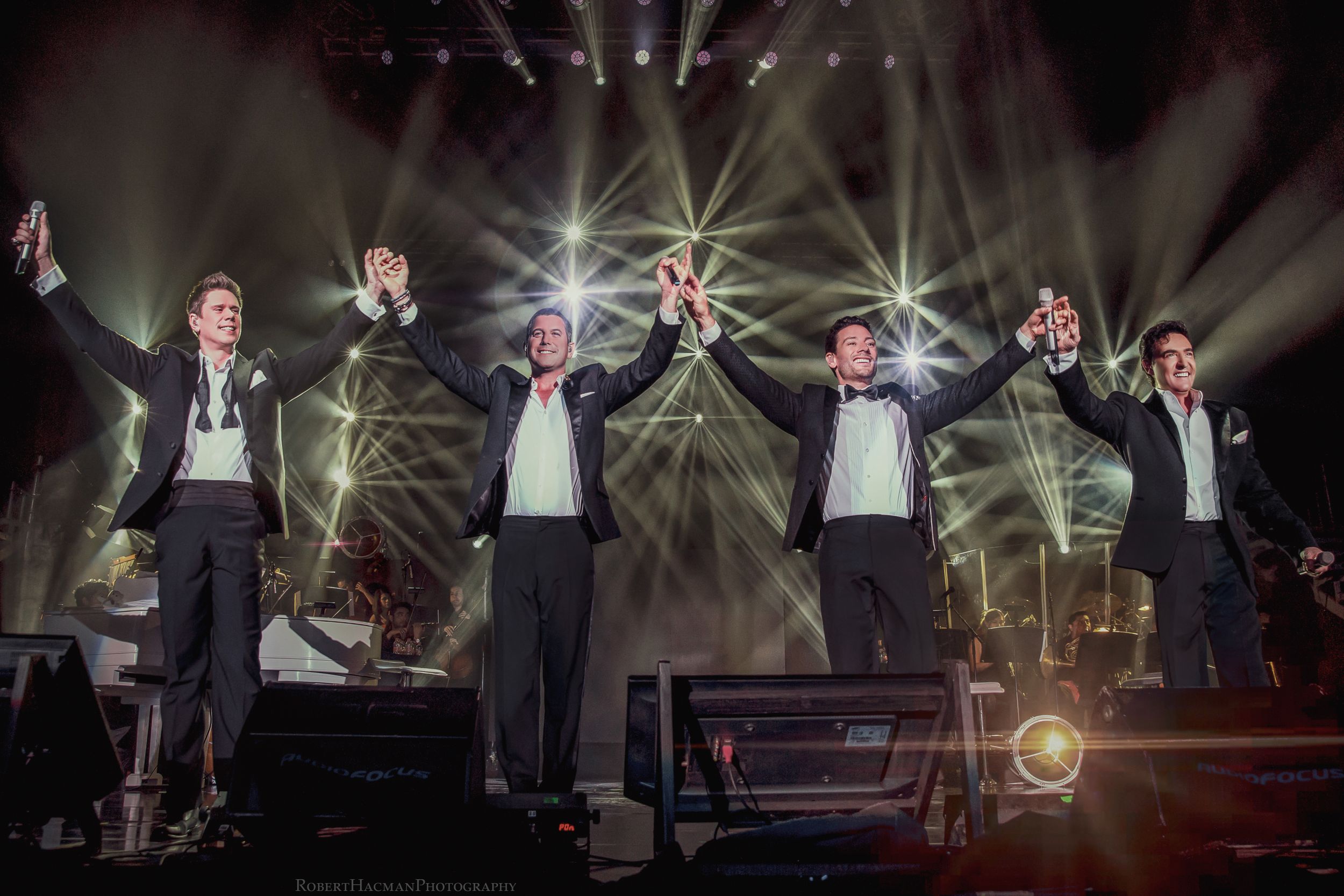 Group performance on illuminated stage with dramatic white lighting and theatrical staging.