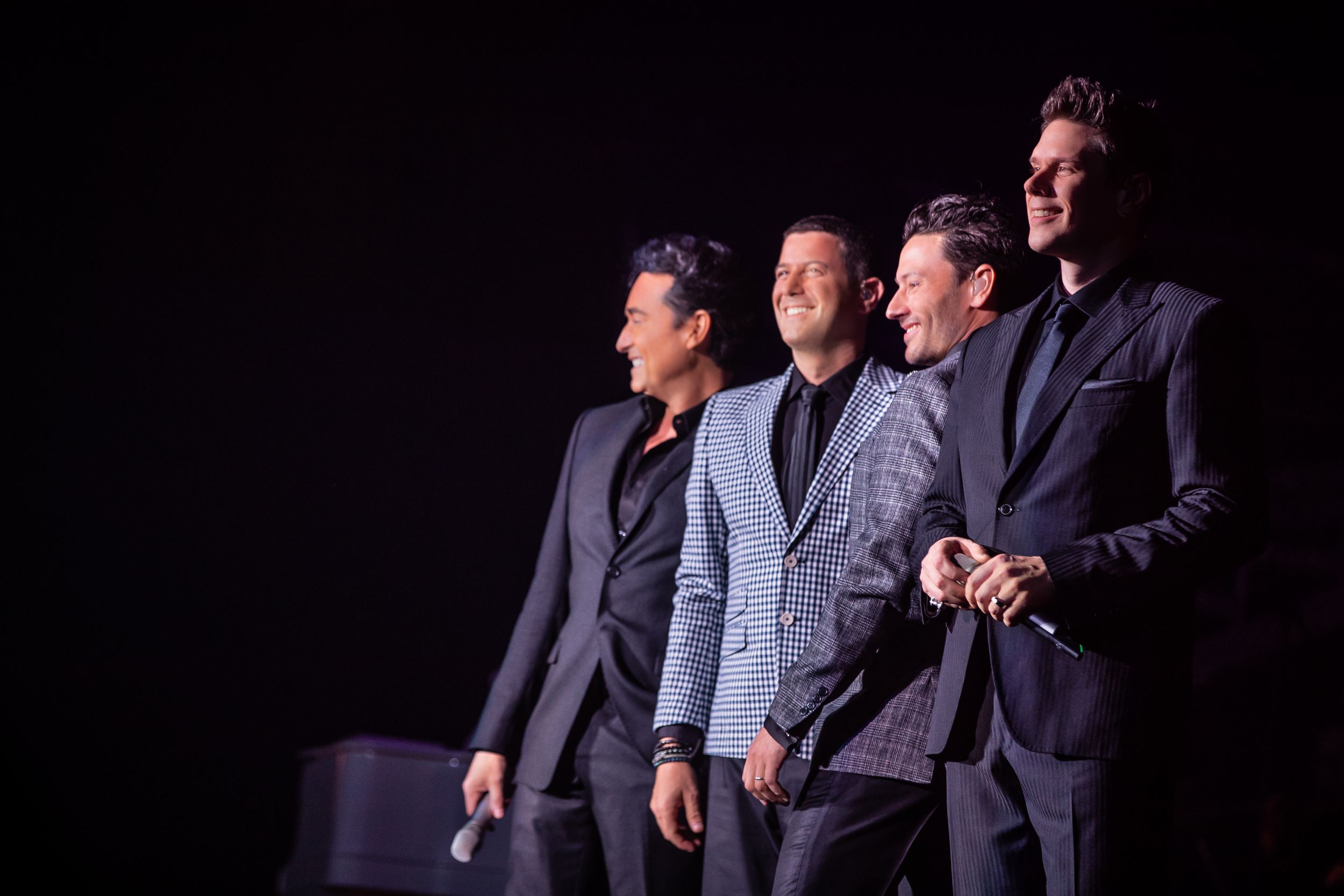 Performers in suits move in coordinated dance sequence on dark stage.