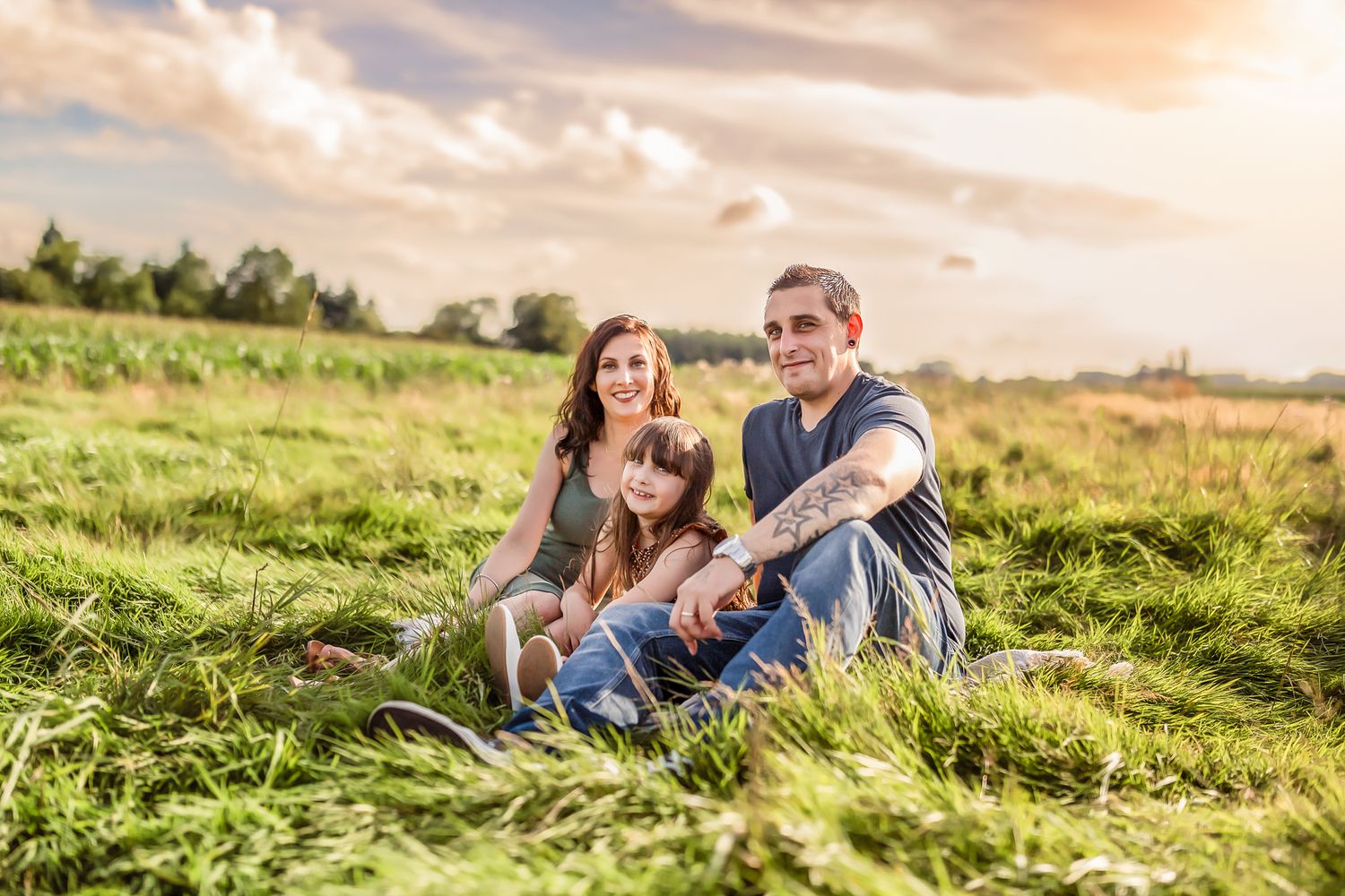 Family with dog relaxing in green grass field during golden hour.