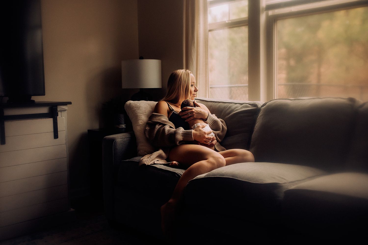 A mother hold her newborn while sitting on the couch during her newborn photo session.
