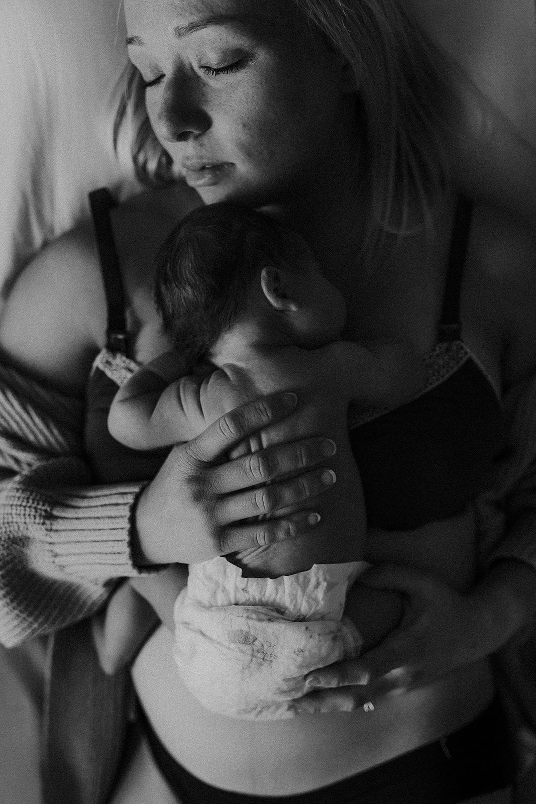 A view looking down as a baby sleeps on her mother's chest while laying in bed.