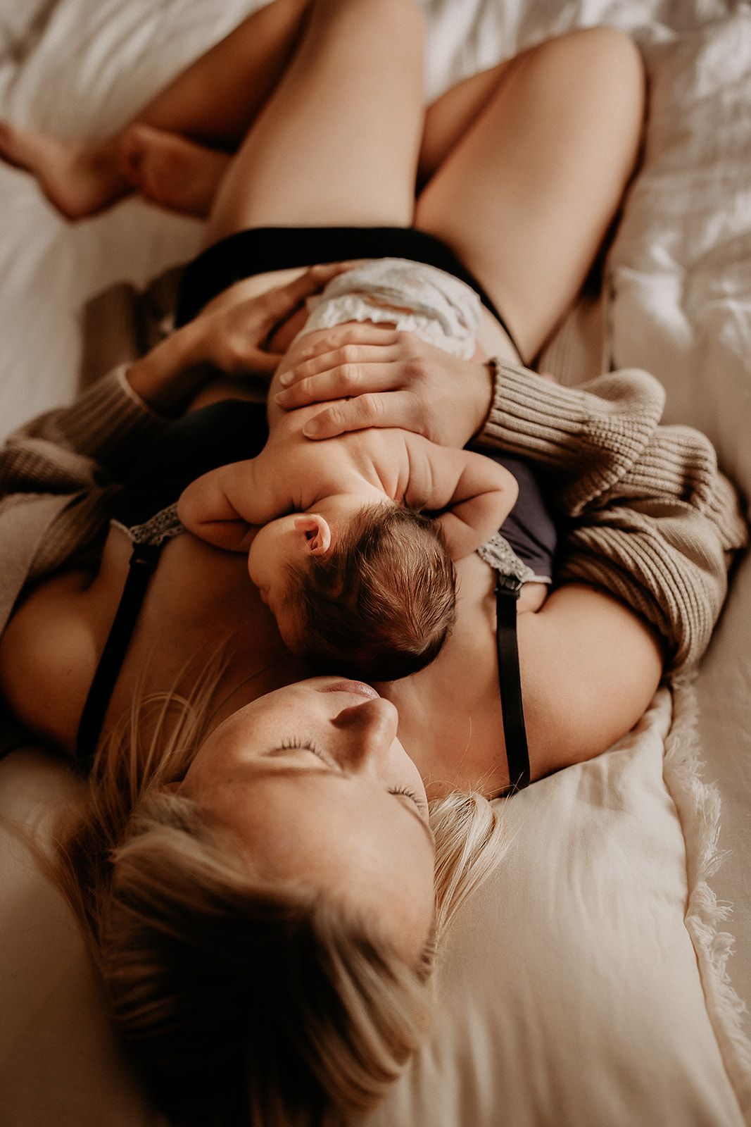 A mother lies on her bed with her baby sleeping on her chest.