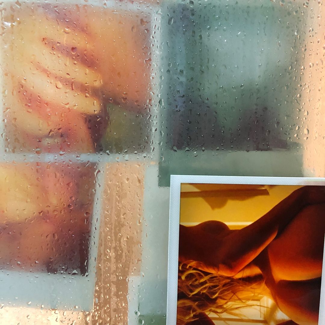 Steamy condensation on glass window panes with a warm-toned photograph displayed in the corner on a rainy day.