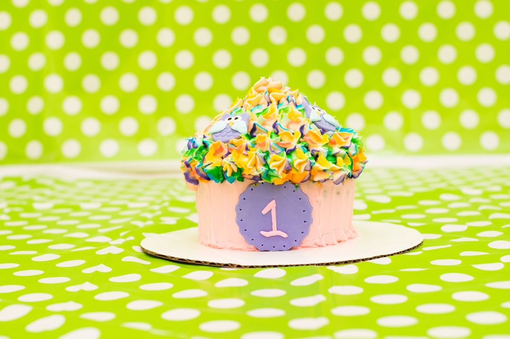 Purple first birthday smash cake with sprinkles on green polka dot background.
