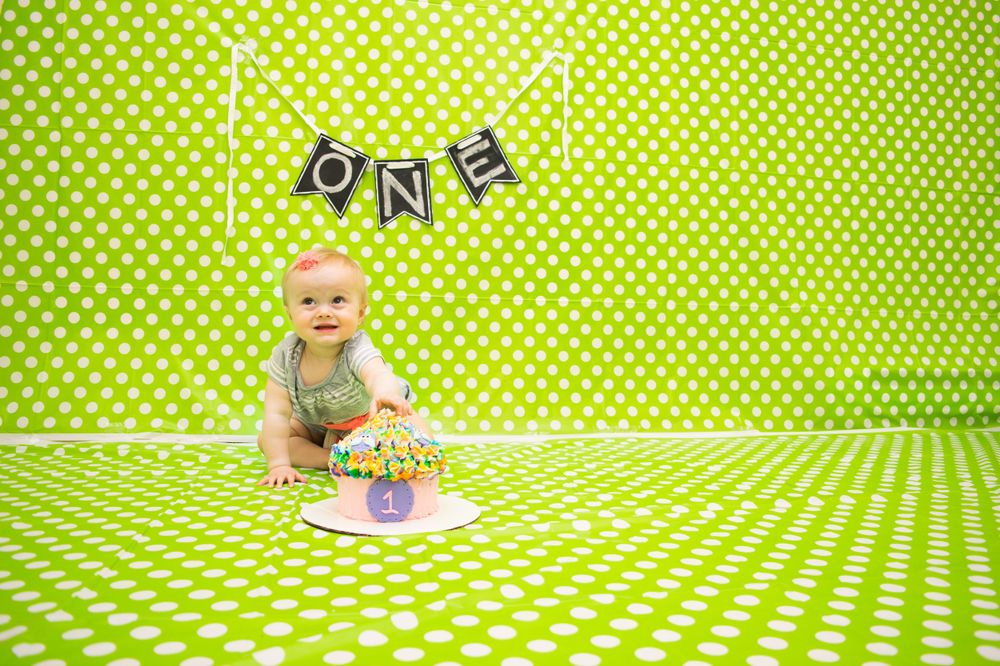 Cake smash photo setup with bright green polka dot backdrop and ONE banner decoration.