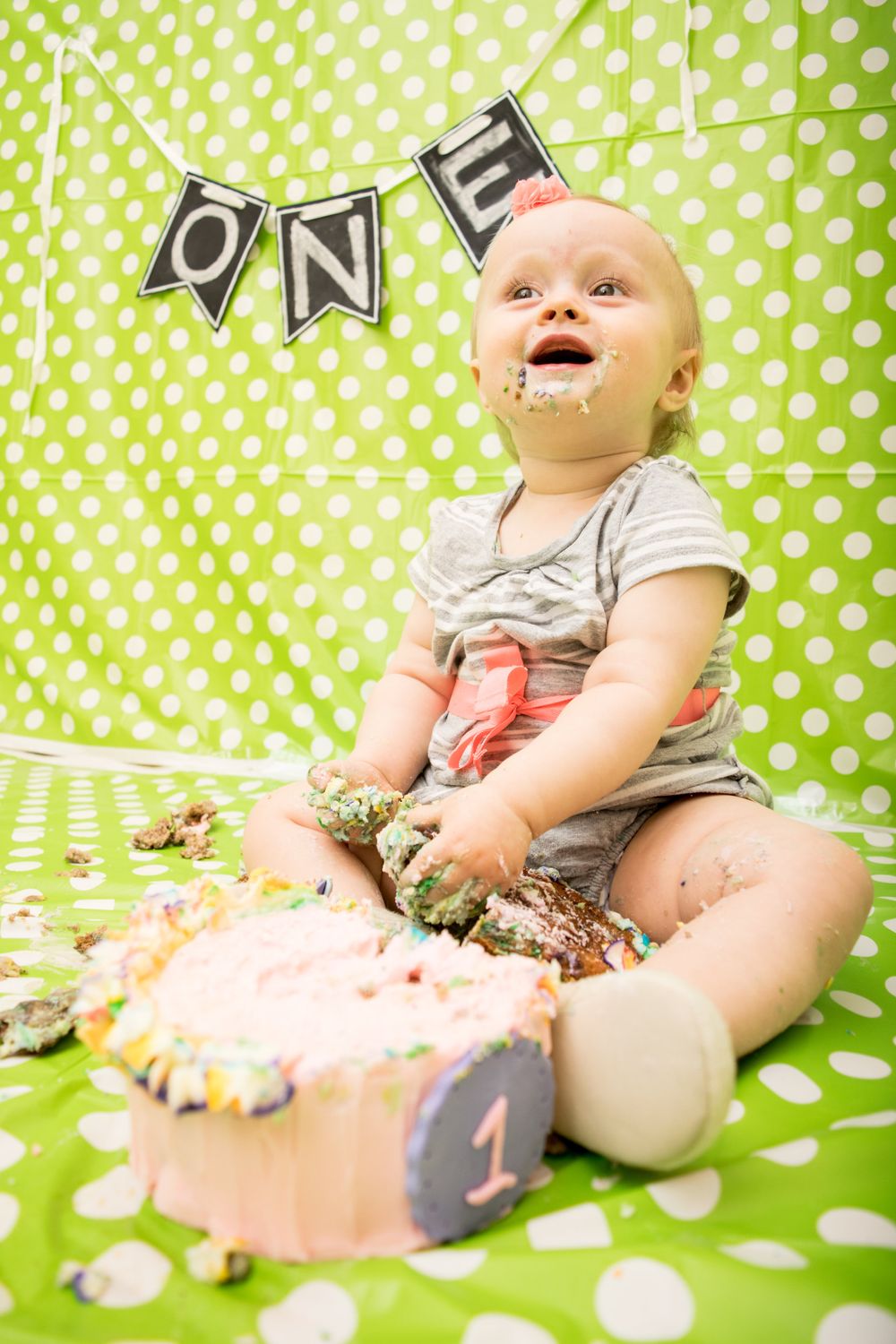 Happy baby enjoying cake smash session with ONE banner and bright green background.