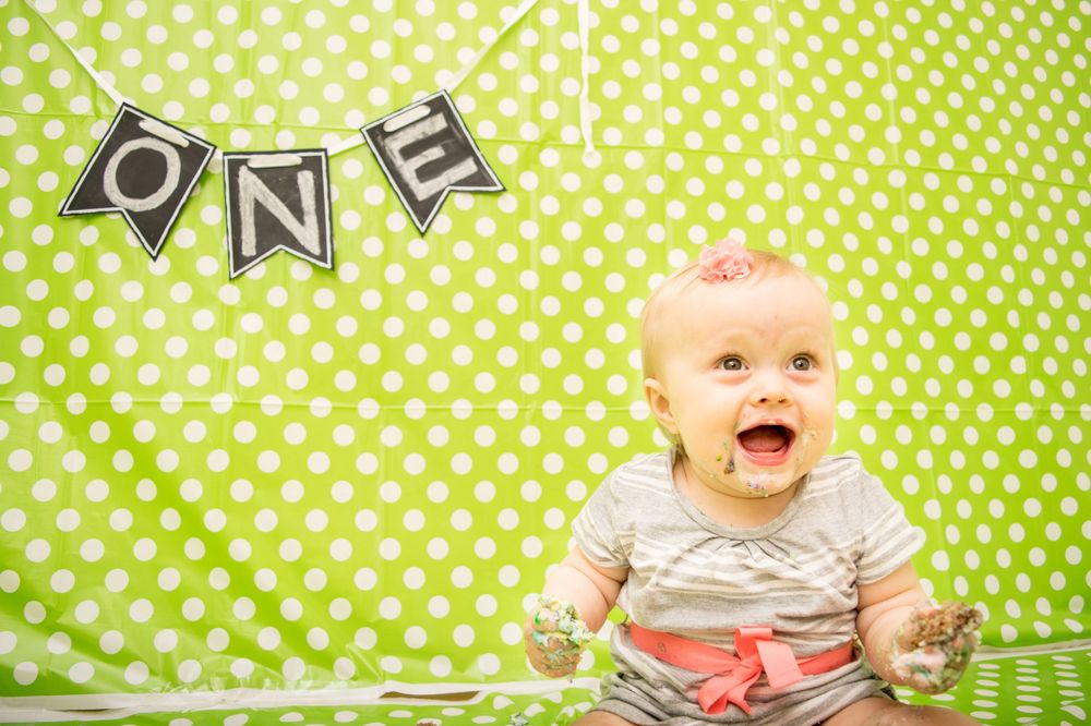 Excited baby celebrating with cake against bright green polka dot background.