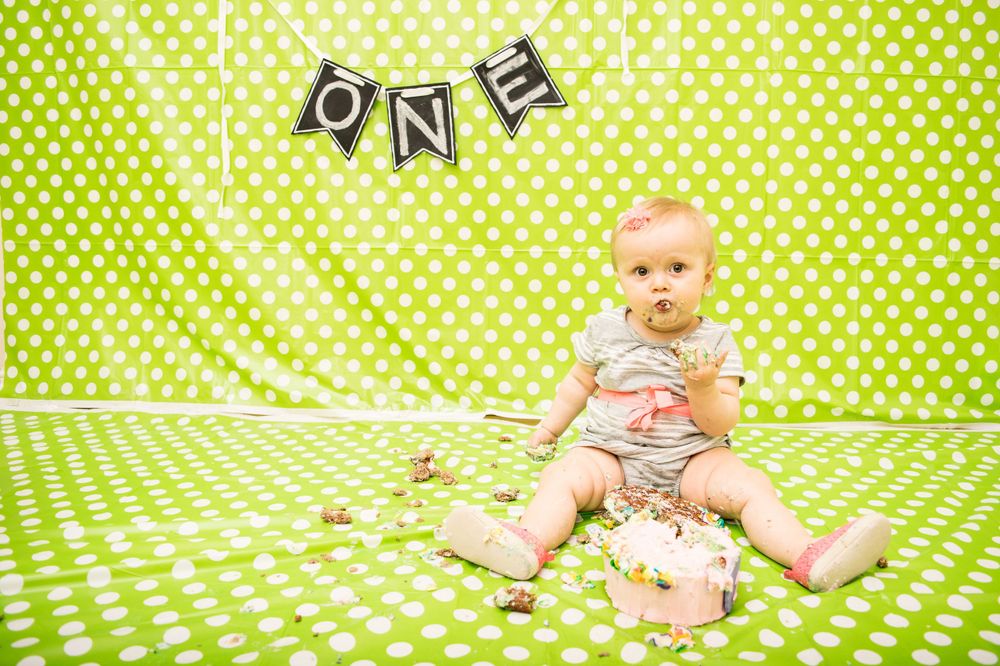 First birthday cake smash photography session with green polka dot backdrop.