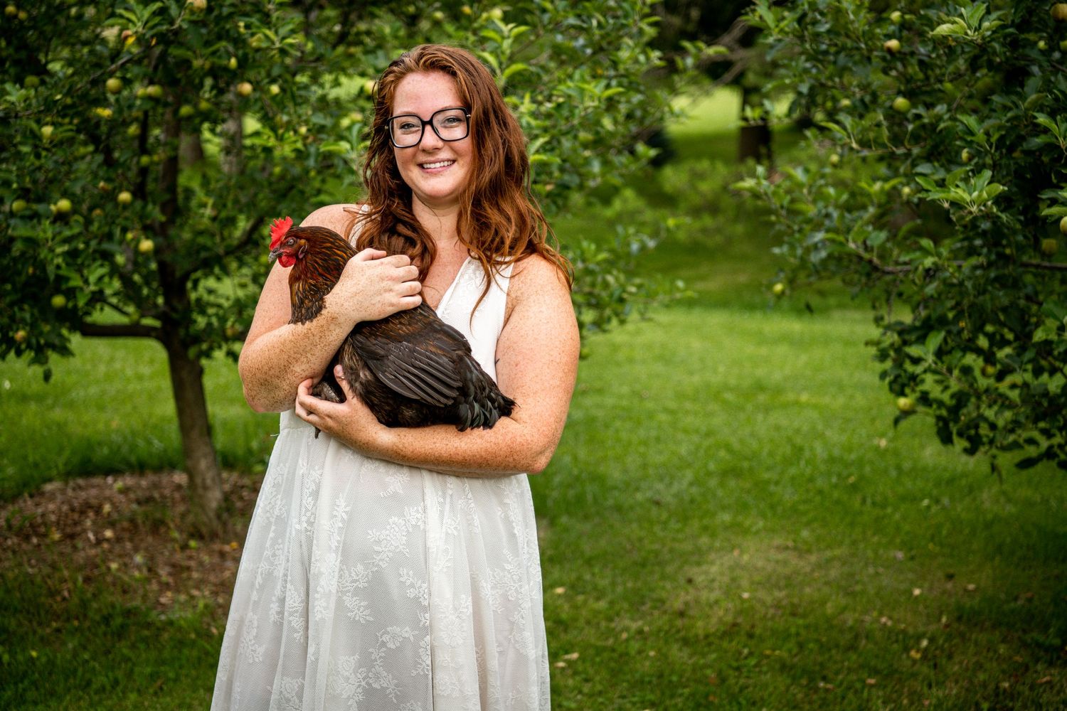 A woman in a white dress holding a chocolate lab puppy in a garden setting.