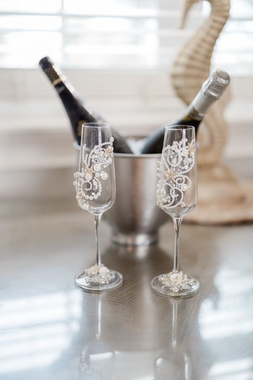Elegant champagne glasses with decorative designs on table with bottles in background.