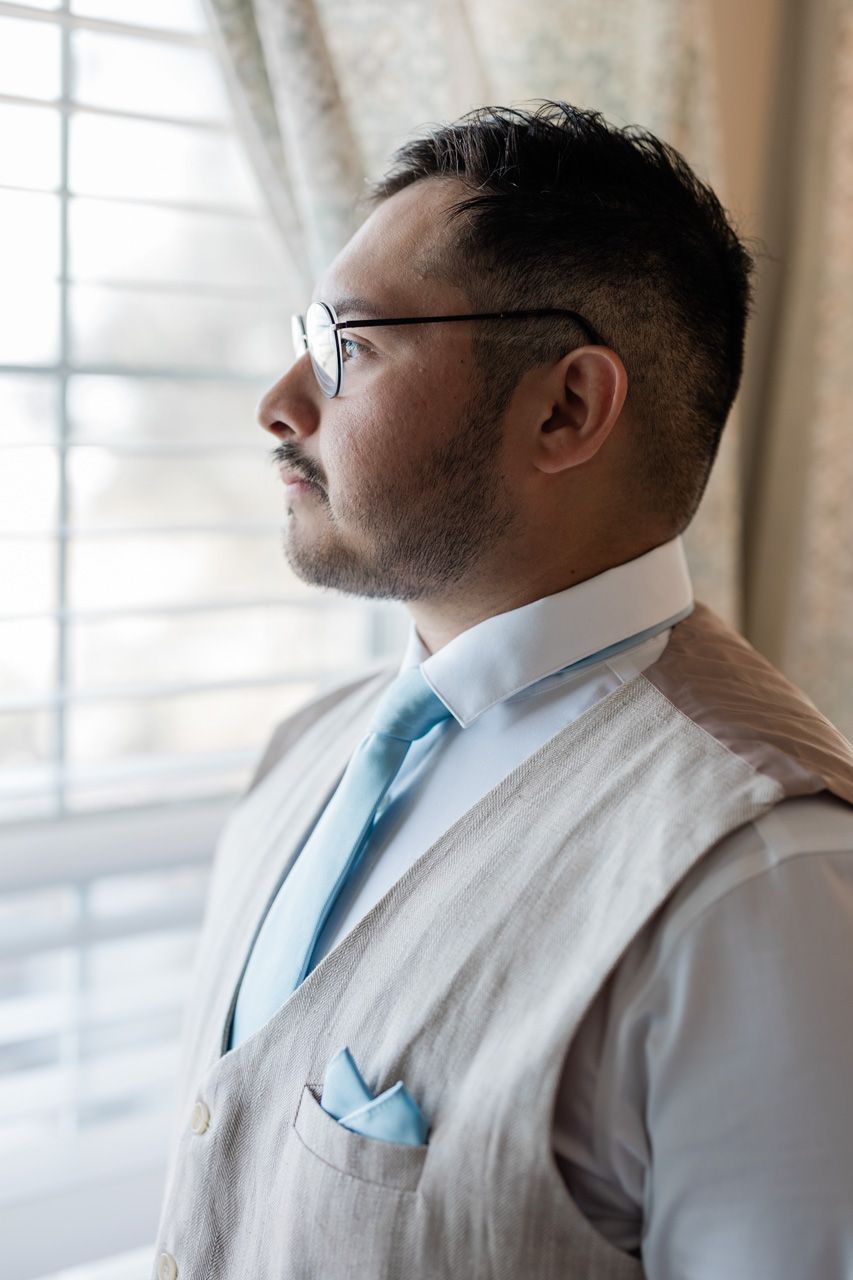 Person in formal attire and glasses looking out window in contemplative pose.