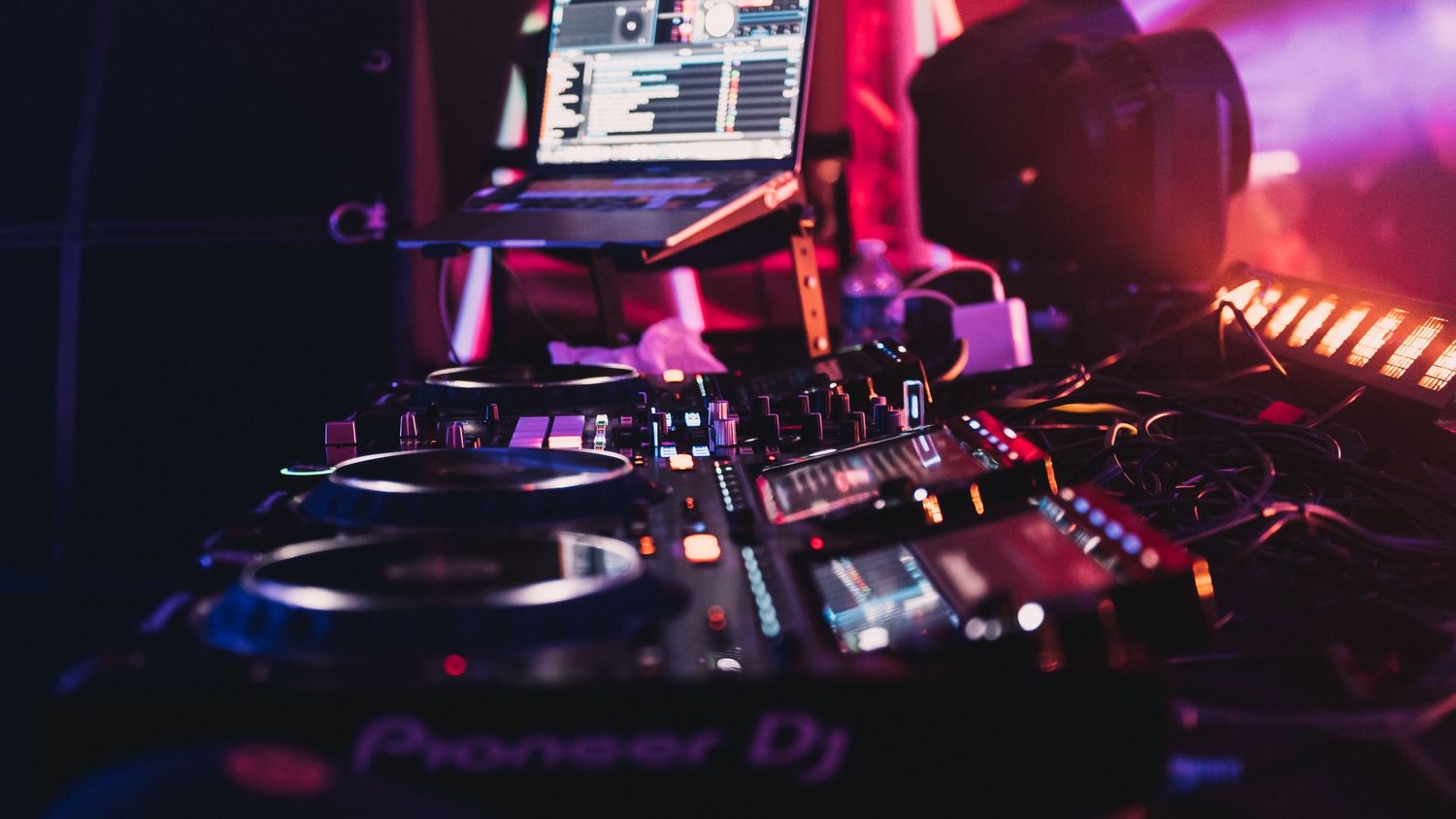 Pioneer DJ controller with turntables and mixer illuminated by colorful purple and pink club lights.