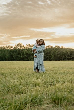 A tender embrace in a sunlit field at golden hour with trees in the background.