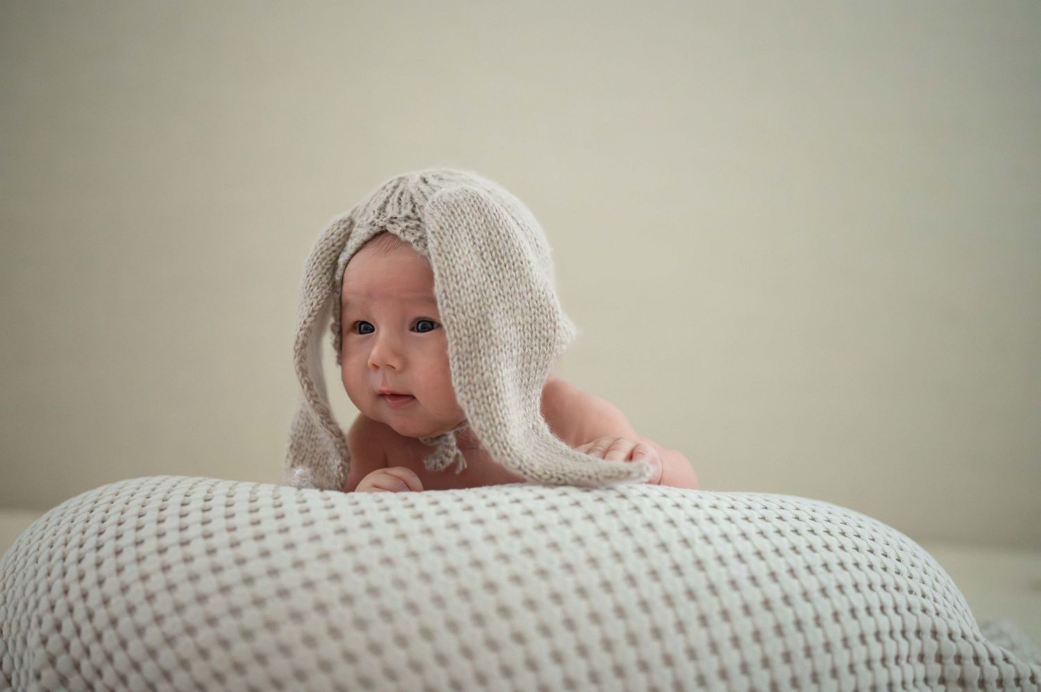 A small baby wrapped in a white towel rests on a polka dot cushion.