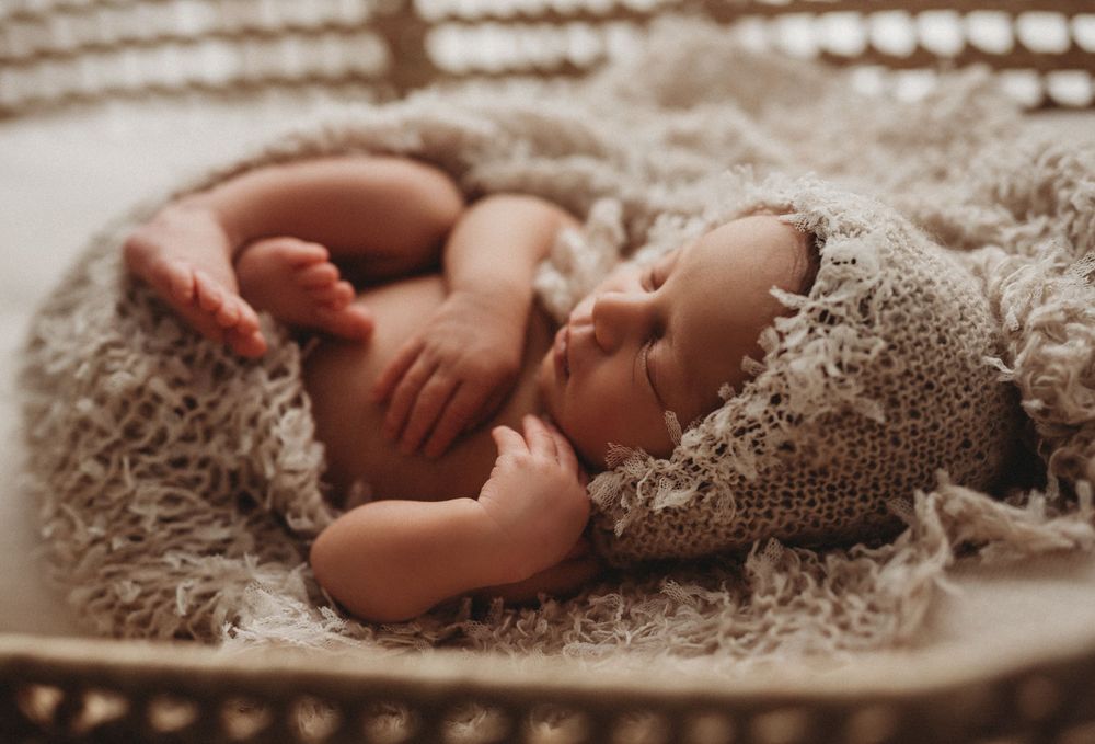 newborn baby girl sleeping in bassinet swaddled with bonnet