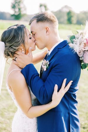 A romantic wedding portrait of a couple sharing their first kiss outdoors with soft lighting.