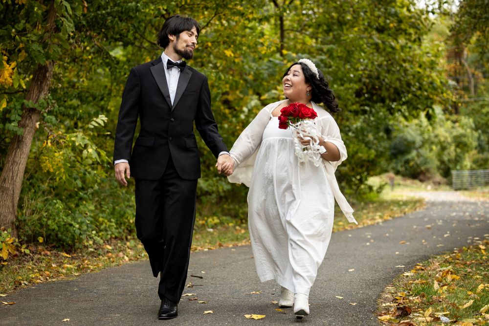 A joyful wedding couple walking together on an autumn path with red roses.