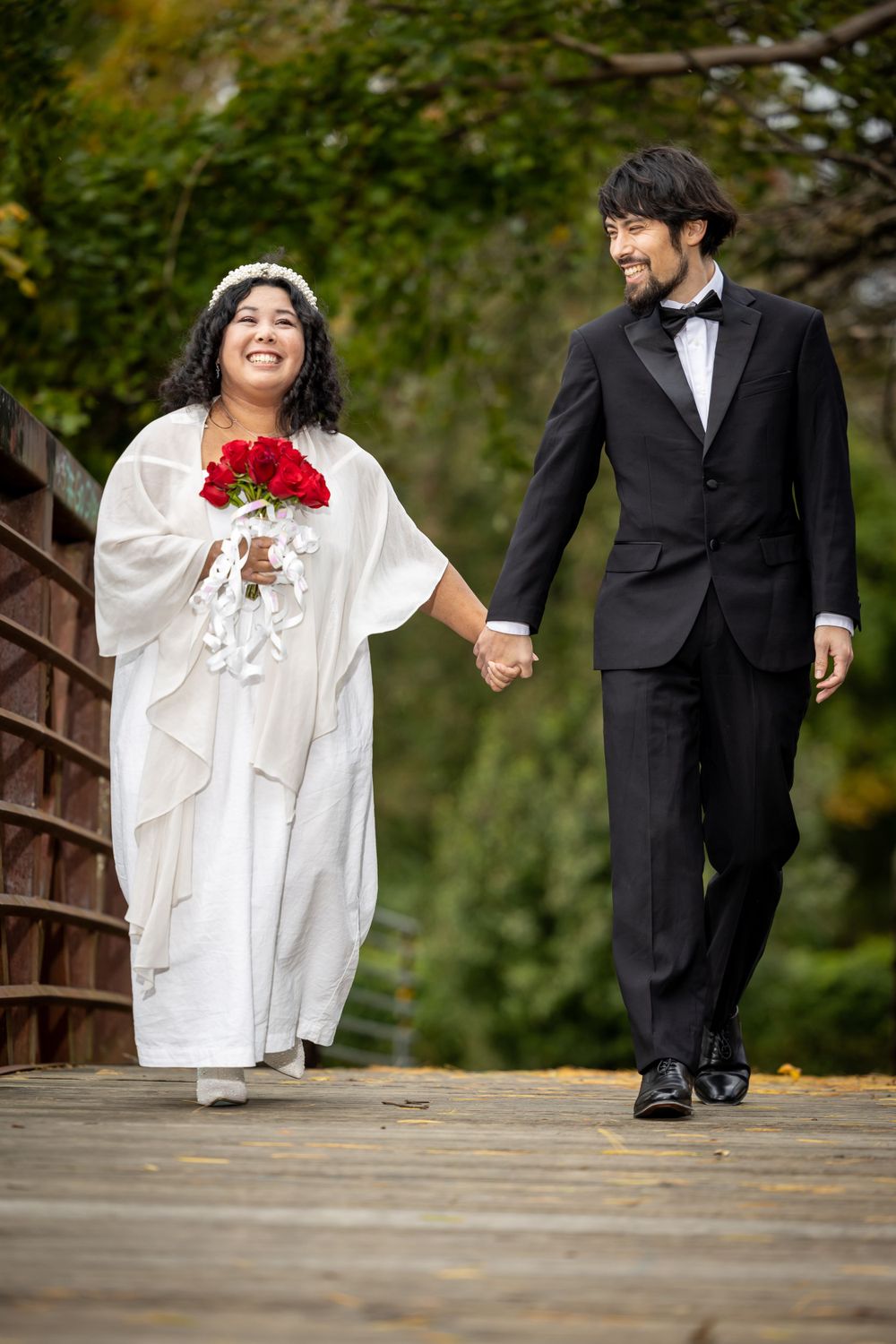 A happy couple walks together on a wooden bridge during their wedding photoshoot.