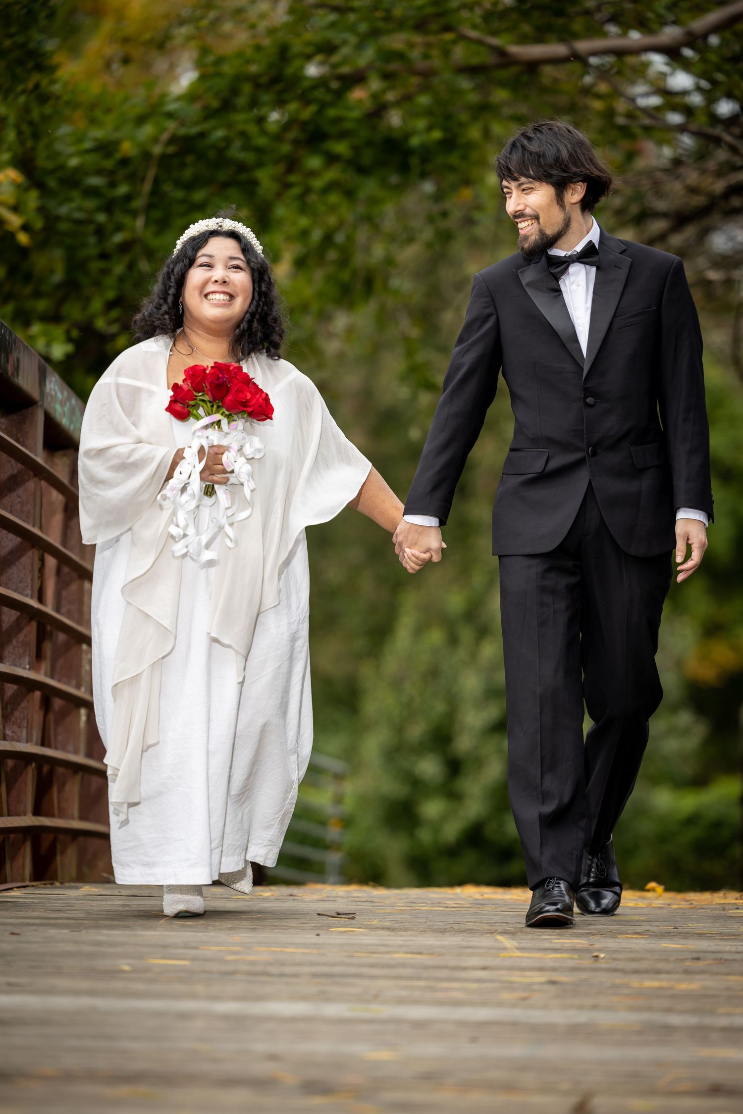 A happy couple walks together on a wooden bridge during their wedding photoshoot.