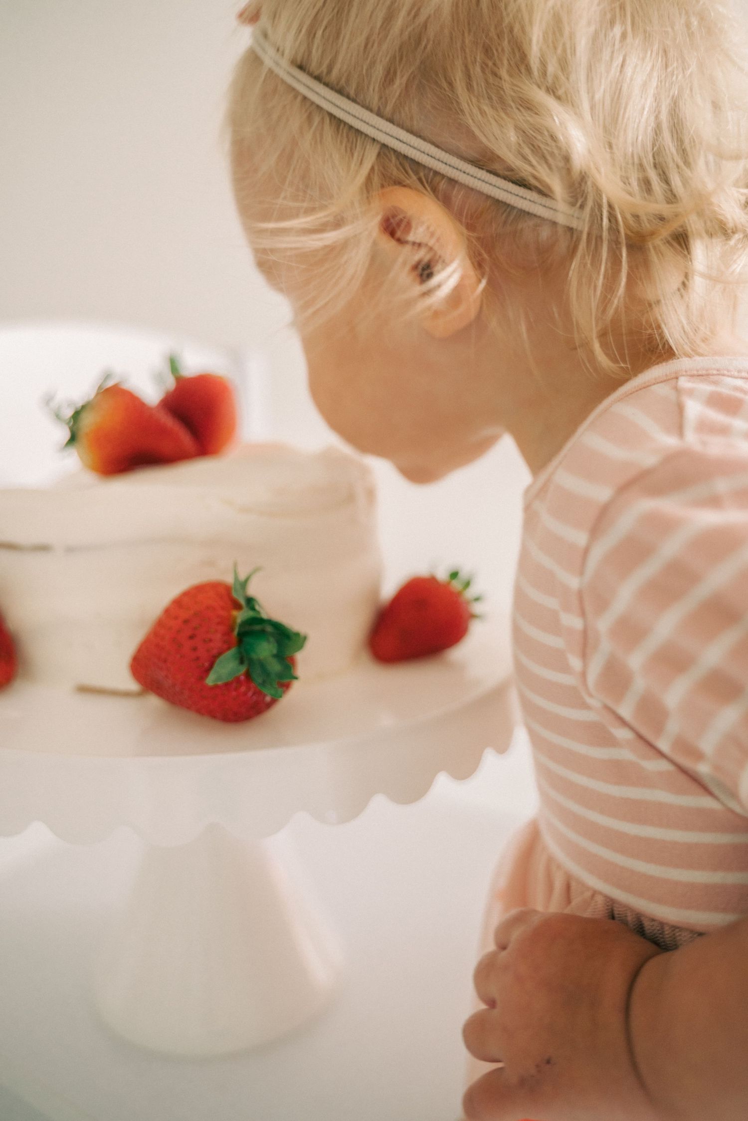 A white frosted cake decorated with fresh strawberries being admired up close.
