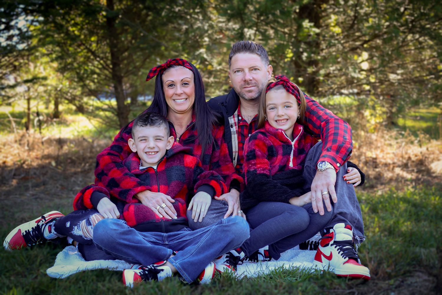 Family in coordinating buffalo plaid outfits relaxing together in a sunny outdoor setting.