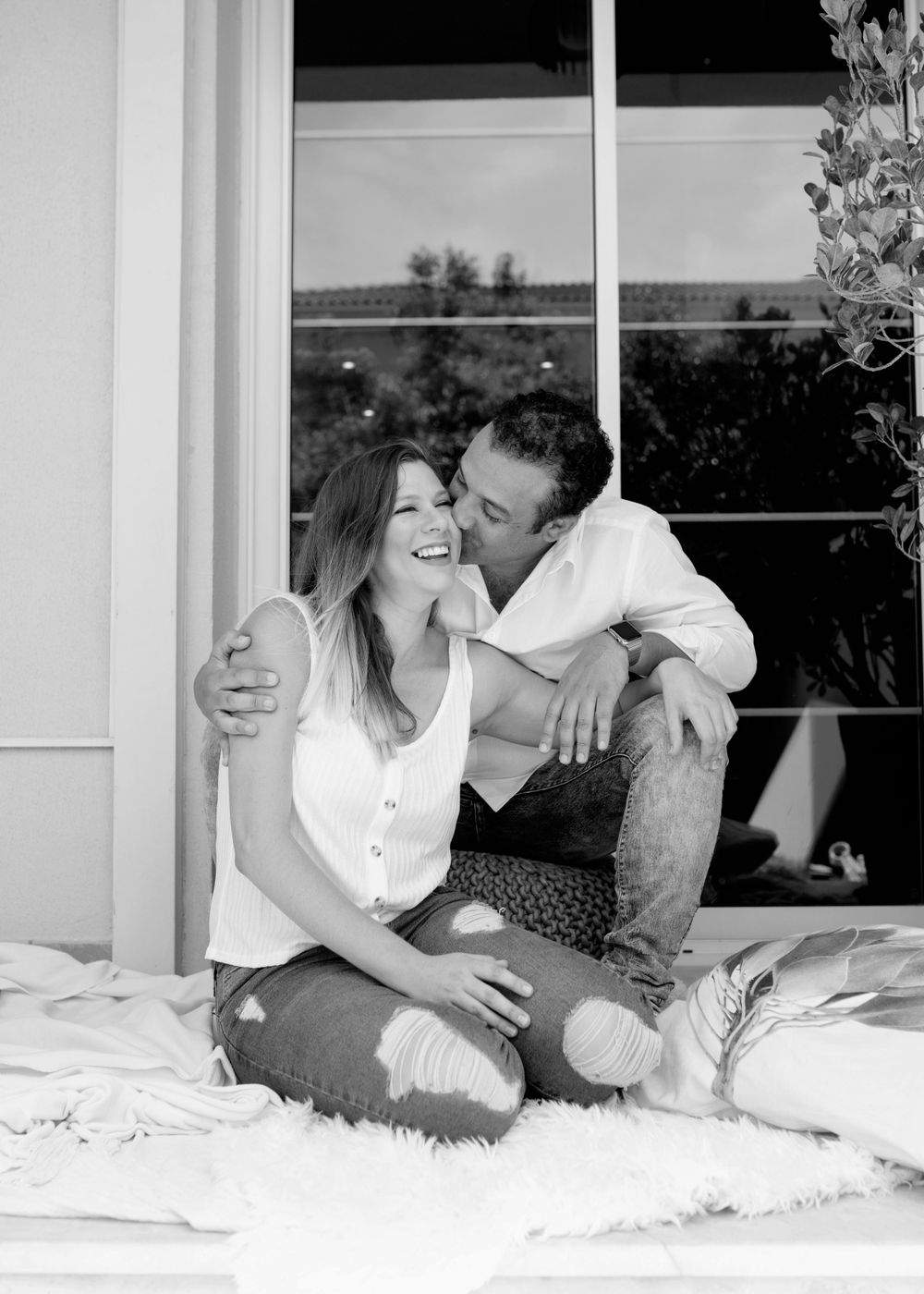 Black and white photograph of a couple laughing together on a windowsill.