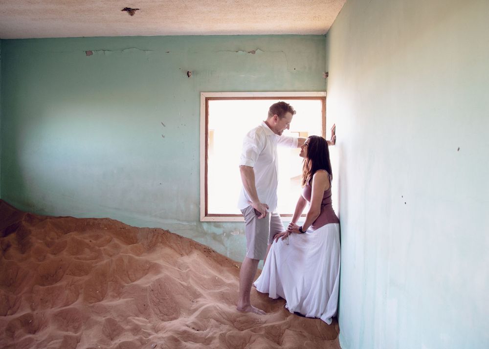 Artistic couple portrait in an abandoned room filled with sand and soft turquoise walls.