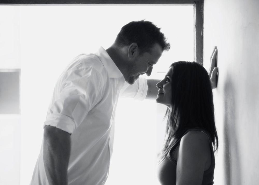 Intimate black and white portrait of a couple in a romantic moment against a light background.