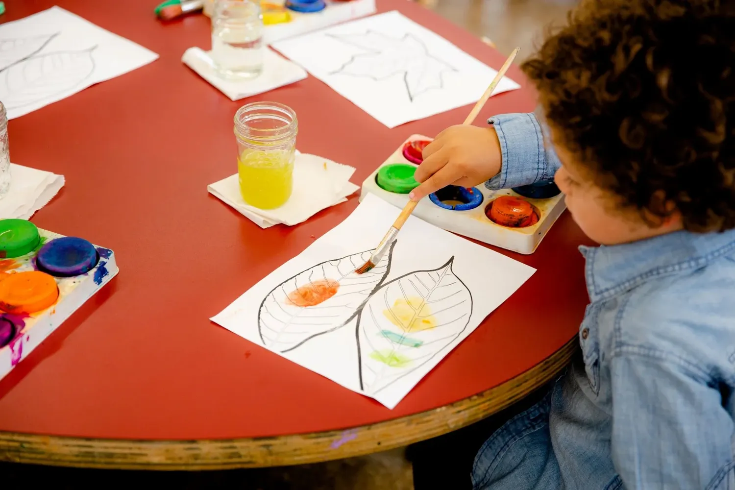Watercolor painting activity with bright paints and paper on a red table.