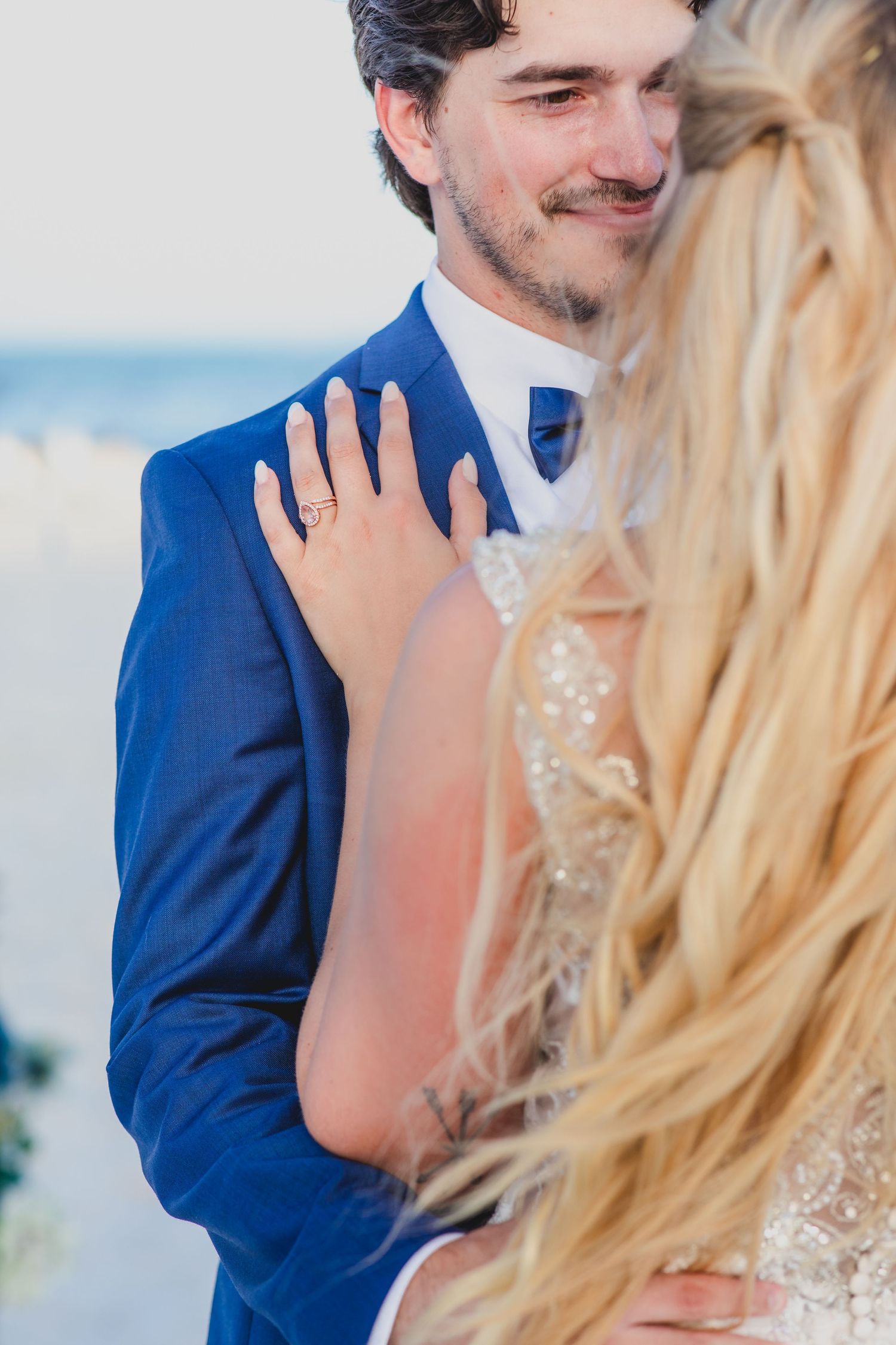 A couple shares an intimate moment during their beach wedding, with the groom wearing a royal blue suit.
