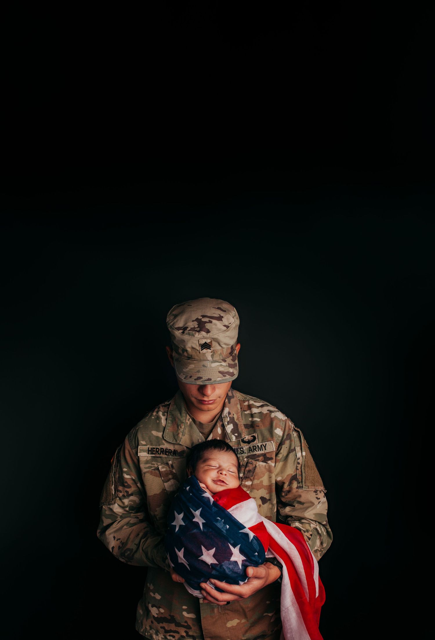Military service member in camouflage uniform holds American flag with infant.
