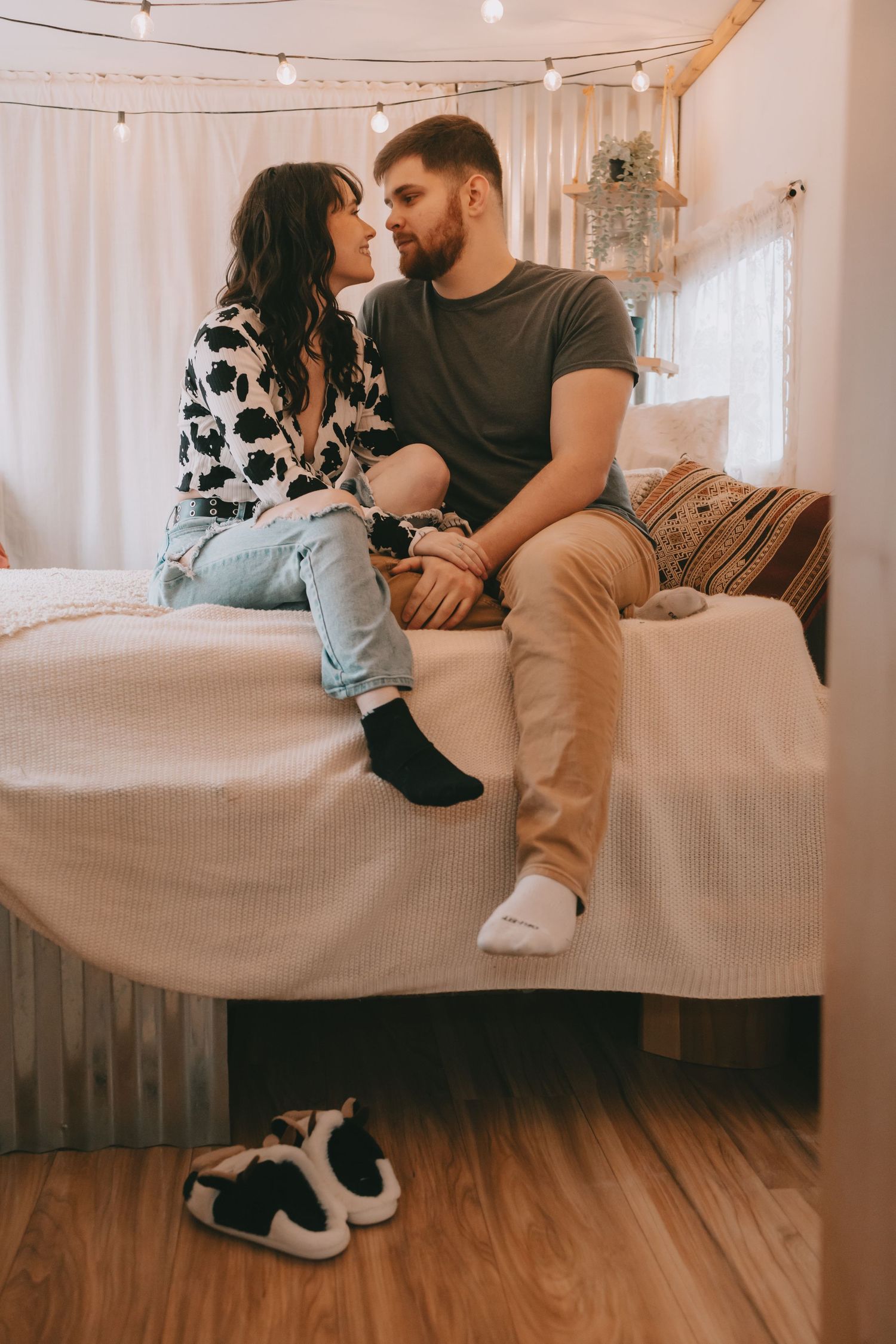 A couple sits on a bed in an embrace looking at each other. Slippers on the floor