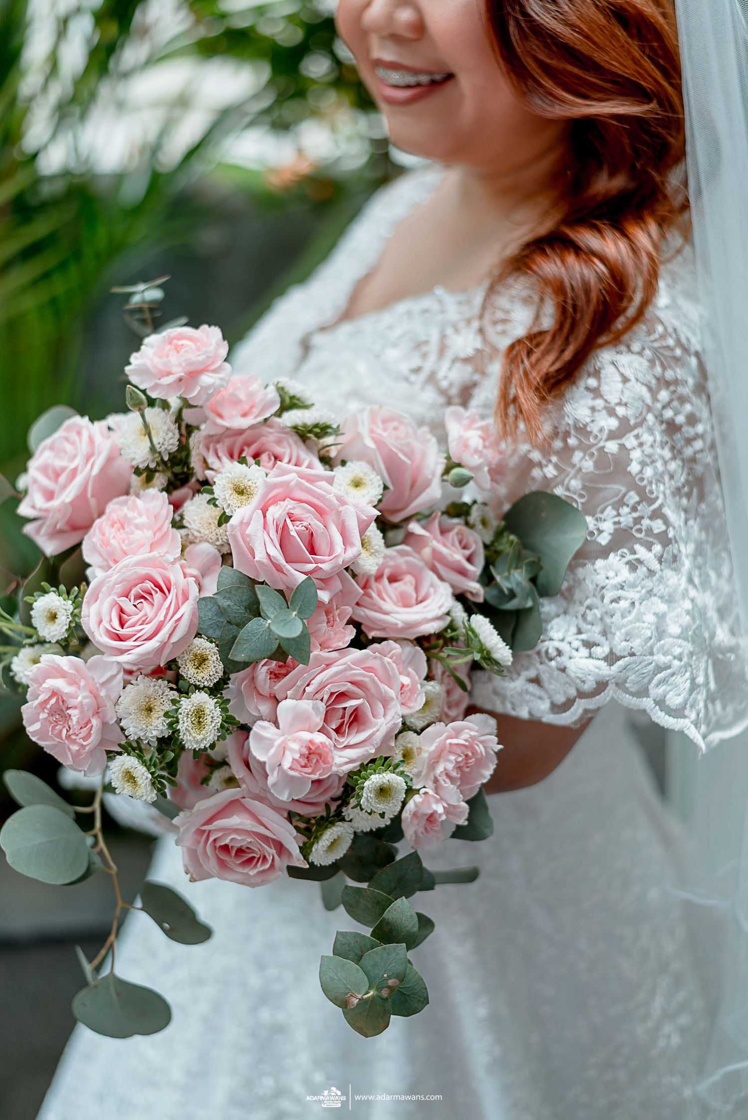 Elegant bridal bouquet featuring soft pink roses and eucalyptus leaves against a white lace wedding dress.