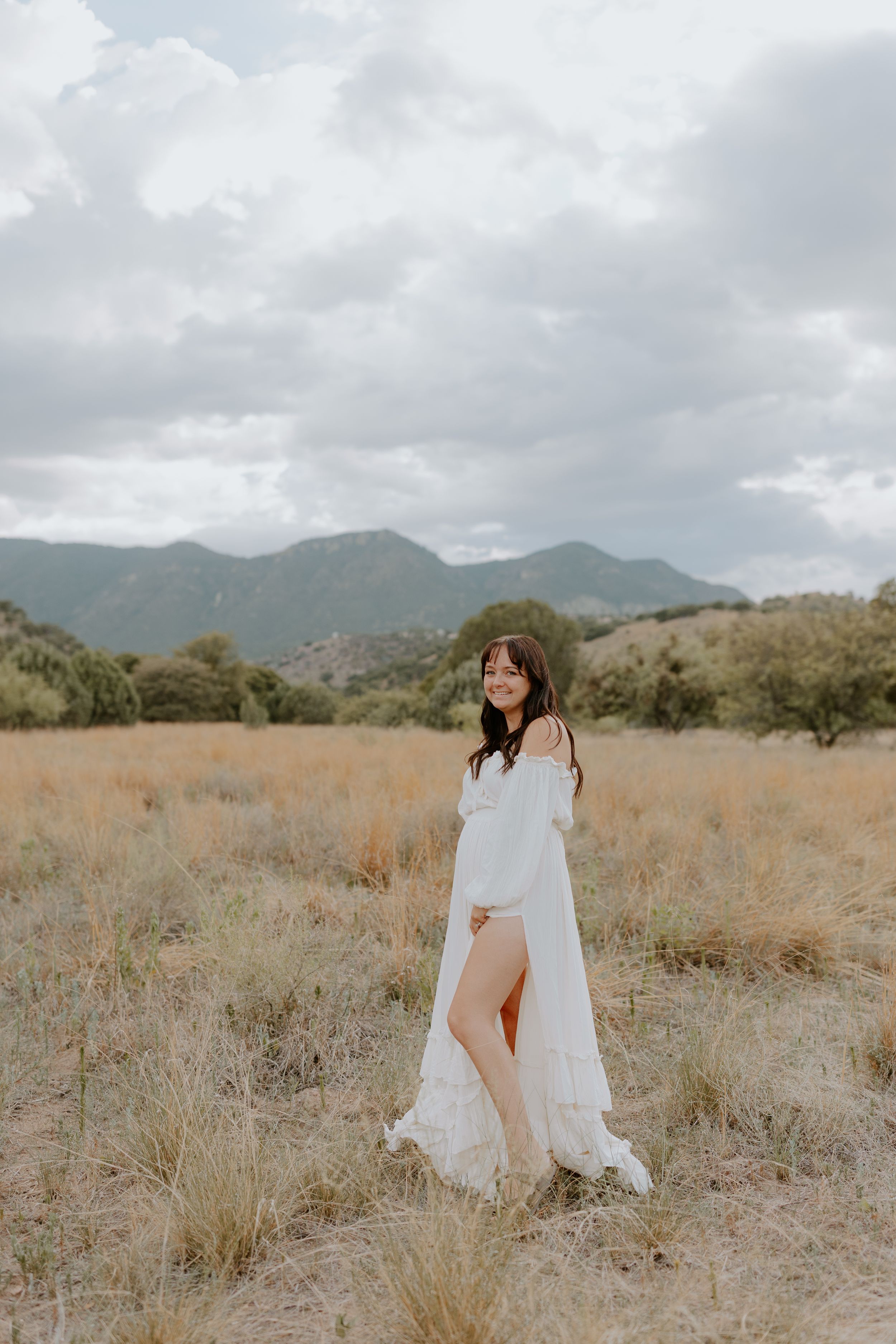 A white flowing dress catches the breeze in a golden field with mountains in the distance.
